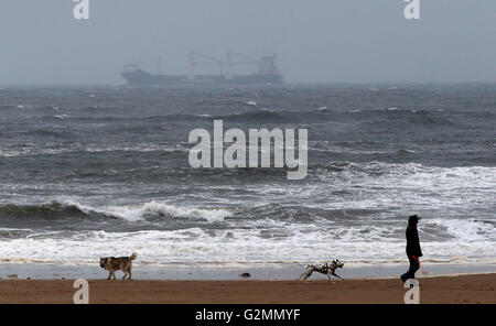 Am ersten Sommertag machen die Menschen einen nassen und windigen Spaziergang am Tynemouth Beach in Tyne & Wear. Stockfoto