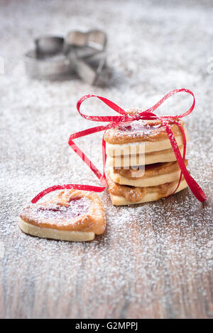 Frische Kekse mit Puderzucker gefüllt mit Marmelade ein Ausstecher im Hintergrund. Stockfoto