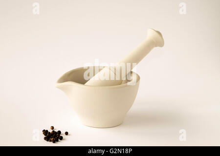 Keramik Mörser und Stößel mit schwarzen Pfefferkörnern auf weißen Hintergrund Stockfoto