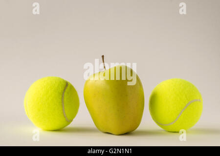 Kuckucksei heraus - glänzend gelber Apfel zwischen zwei Tennisbälle auf weißen Hintergrund Stockfoto