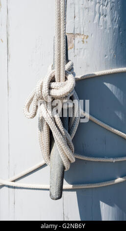 Seil geschlungen mehrmals um vertikale Klampe und abgebunden, wirft Schatten auf gemalten weißen Holz Mast. Stockfoto