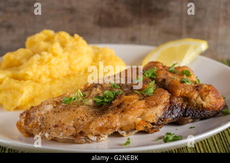 Gebratener Fisch mit Polenta und Zitrone auf Platte Stockfoto