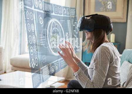 Frau sitzt auf dem Sofa zu Hause tragen Virtual-Reality-Kopfhörer Stockfoto