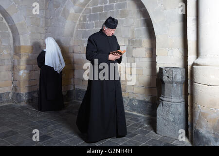 Priester, eine junge Nonne entlang der Mauern des mittelalterlichen Klosters vorbei Stockfoto