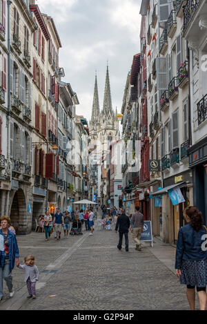 Menschen wandern in Rue Pont Neuf Rue de Bayonne mit Kathedrale Sainte-Marie de Bayonne im Hintergrund. Aquitaine, Frankreich. Stockfoto