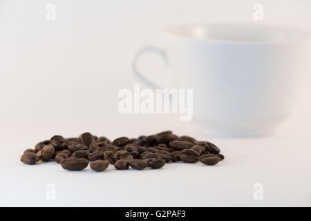 verschüttete Kaffeebohnen mit weißen verschwommen Tasse im Hintergrund Stockfoto
