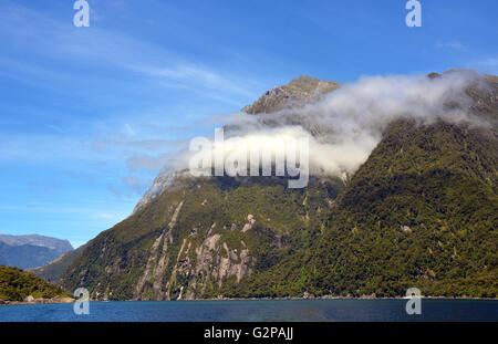 Niedrige Wolken hängen rund um den steilen hohen Klippen am Milford Sound, in glazialen Fiordland, Südinsel, Neuseeland Stockfoto