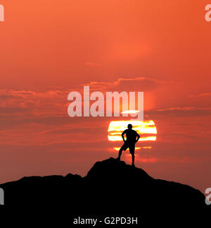 Sonnenuntergang Landschaft mit Silhouette eines Kletterers stehend mit Rucksack auf dem Hintergrund der Sonnenscheibe und bunten roten Himmel in Summe Stockfoto