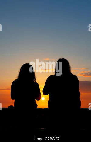 Sunrise Silhouette Southport, Merseyside, Großbritannien. Juni 2016. Zwei Schwestern haben sich gegen die untergehende Sonne über Southport geschilhoutet, als sie das Beste aus der Sommerhalbzeit der Schule in der Abenddämmerung machen. Stockfoto