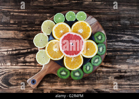 Orangen- und Grapefruitsaft Scheiben angeordnet auf einem Teller in Form einer Blume mit mehr Scheiben von Kiwi, Zitrone und Limette. Draufsicht mit Kopie Stockfoto