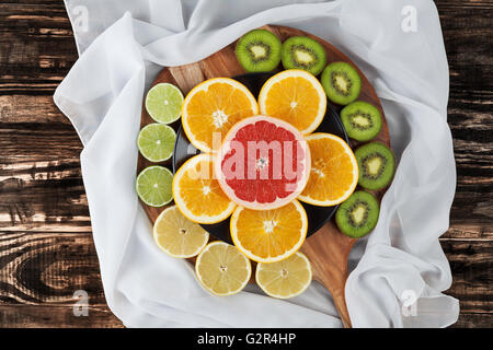 Scheiben von Zitrusfrüchten angeordneten runden Schneidebrett mit eleganten Seidentuch. Ansicht von oben. Stockfoto