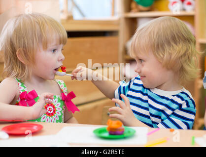 Zwei Kinder spielen im Kindergarten zusammen. Junge Fütterung Mädchen. Stockfoto