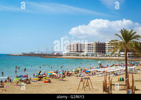 Sonnenstrand Playa del Postiguet nahe der Burg Santa Barbara. Touristen entspannen Sie unter Sonnenschirmen auf dem warmen Sand. Alicante, Spanien Stockfoto