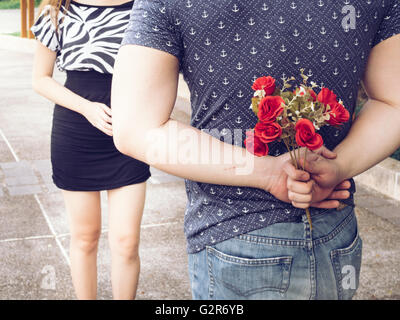 Junger Mann versteckt Rosen aus seinem zurück und geben sie an seine Freundin. Stockfoto