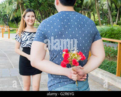 Junger Mann versteckt Rosen aus seinem zurück und geben sie an seine Freundin. Stockfoto