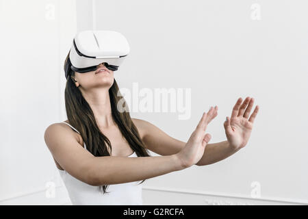 Eine junge weiße Frau mit dunklen Haaren steht mit zu fühlen und zu spüren, mit einer virtuellen Realität Heasdet auf dem Kopf ausgestreckten Armen Stockfoto