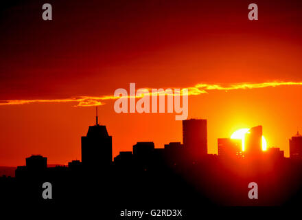 Große, leuchtende orange Sonnenuntergang hinter Stadtgebäude Silhouette unter einem roten und orangefarbenen Himmel Stockfoto