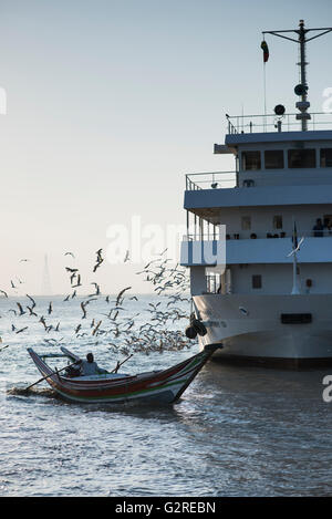 Ein traditionelles langes Boot vorbei an eine Passagierfähre am Yangon Fluss in Yangon, Myanmar. Stockfoto