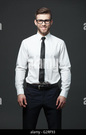 Porträt von hübscher junger Geschäftsmann gegen dunkelgrauen Hintergrund stehend. Stockfoto