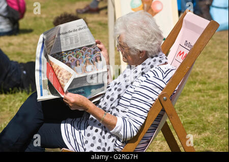 Ältere Dame lesen Zeitung setzte sich im Liegestuhl auf der Wiese bei Hay Festival 2016 Stockfoto