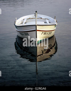 Ein kleines offenes Boot spiegelt sich im flachen, klaren, blauen Wasser an der Costa Brava von Spanien. Stockfoto