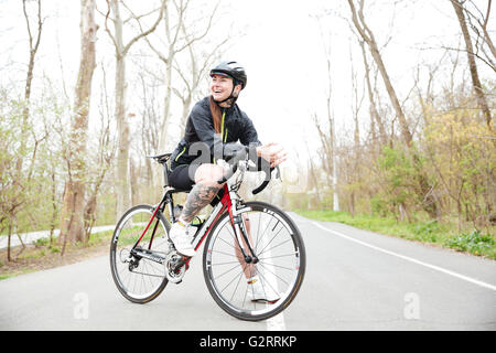 Voller Länge des Lächelns tätowierten junge Frau im Helm beim Fahrrad stehen auf der Straße im park Stockfoto