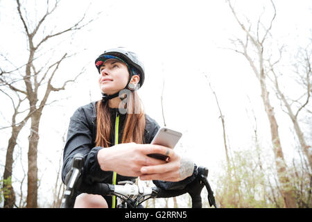 Porträt der nachdenkliche junge Frau auf dem Fahrrad mit Handy im park Stockfoto