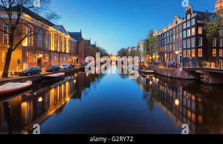 Schöne Nacht Stadtbild in Amsterdam, Niederlande. Die Lichter der Stadt in Wasser mit blauer Himmel wider. Nachtbeleuchtung des Gebäudes Stockfoto