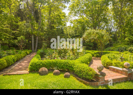 schön angelegter Garten mit Buchsbaum, Bäume, Rosen und einem Ziegelsteinweg Stockfoto