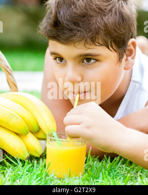 Portrait eines glücklich Teen jungen auf frischen grünen Wiese liegend und trinken lecker Saft, Bananen essen Stockfoto