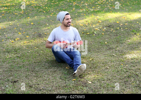 Porträt von schönen jungen Mann spielen der Ukulele in einem Park. Im Freien. Stockfoto