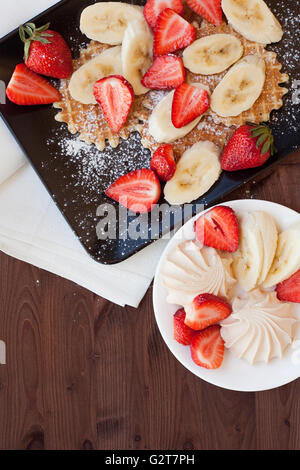 Waffeln mit frischen Erdbeeren und Bananen auf rustikalen hölzernen Hintergrund. Ansicht von oben Stockfoto
