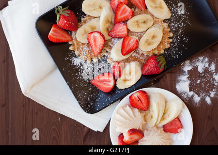Waffeln mit frischen Erdbeeren und Bananen auf rustikalen hölzernen Hintergrund. Ansicht von oben Stockfoto