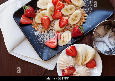 Waffeln mit frischen Erdbeeren und Bananen auf rustikalen hölzernen Hintergrund. Ansicht von oben Stockfoto