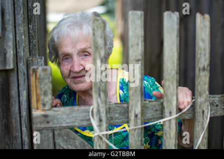 Eine ältere Frau blickt hinter einem Zaun im Dorf. Stockfoto