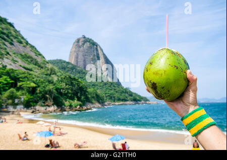 Brasilianische Sportler halten frische Coco Gelado grüne Kokosnuss gegen die Ansicht der Guanabara-Bucht und Zuckerhut, Rio zu trinken Stockfoto