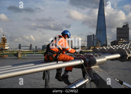 Ein Ingenieur führt wesentliche Wartung am Rande der Millennium Bridge in London, gegenüber The Shard. Stockfoto