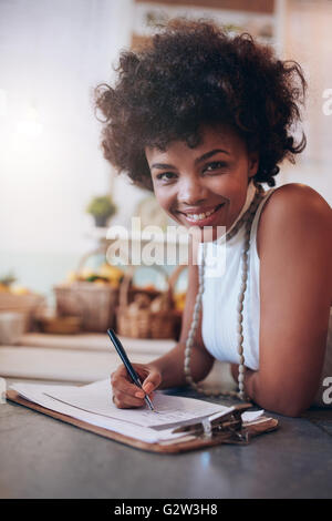 Porträt der lächelnde junge Frau in eine Saftbar und Schreiben von Notizen. Afrikanische Frauen stehen hinter der Theke zu betrachten Stockfoto