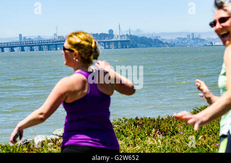 Zwei Damen, für einen Spaziergang auf der Marina-Park-Bahn an der Powell Street in Emeryville mit der Bay Bridge und San Francisco Stockfoto