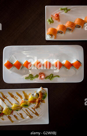 Vielzahl von bunten Sushi-Rollen über eine dunkle Tischplatte auf verschiedenen Tellern serviert. Stockfoto