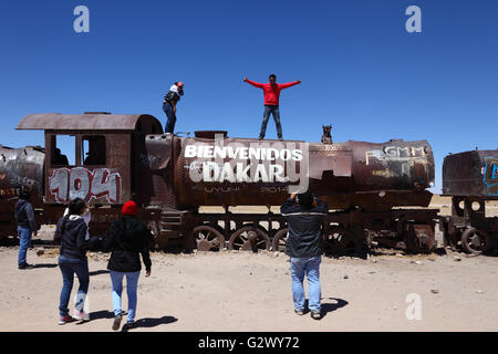 Student, posiert für Fotos auf alte Dampfmaschine mit willkommen Dakar Graffiti gemalt, Uyuni Zug Friedhof, Bolivien Stockfoto