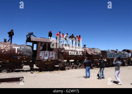 Studenten, posiert für Fotos auf alte Dampfmaschine mit willkommen Dakar Graffiti gemalt, Uyuni Zug Friedhof, Bolivien Stockfoto