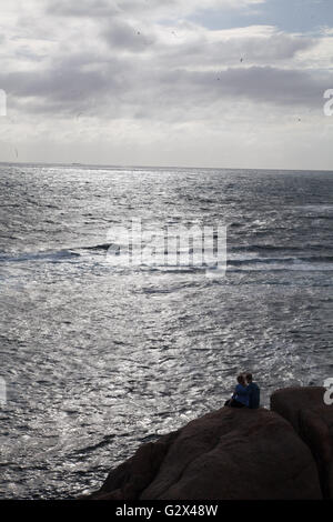 zwei Menschen sitzen an der felsigen Küste beobachten das Meer vor der Küste von Cape Leeuwin, Western Australia Stockfoto