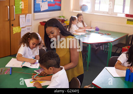 Weibliche Grundschullehrerin helfen Schülern am Schreibtisch Stockfoto