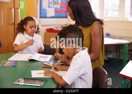 Weibliche Grundschullehrerin helfen Schülern am Schreibtisch Stockfoto