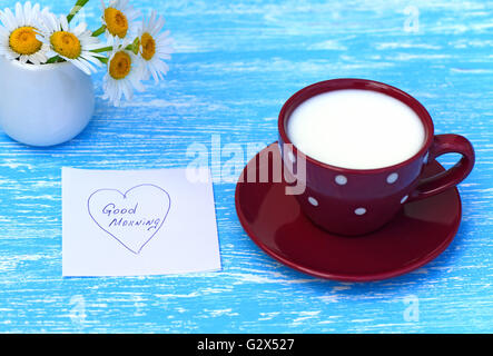 Blumen-Gänseblümchen und eine Tasse Milch mit beachten Sie guten Morgen auf rustikalen hölzernen Hintergrund Stockfoto