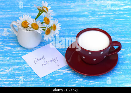 Blumen-Gänseblümchen und eine Tasse Milch mit beachten Sie guten Morgen auf rustikalen hölzernen Hintergrund Stockfoto