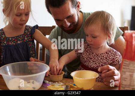 Vater mit Töchtern Backen zu Hause Kuchen zusammen Stockfoto