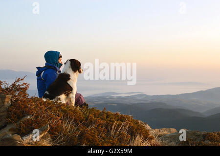 Junge Frau mit Hund gerade Sonnenaufgang hoch in den Bergen Stockfoto