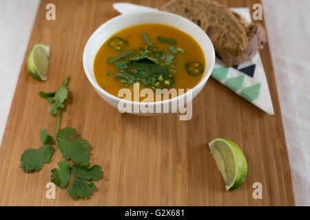 Frisch zubereitete Karotten und Koriander-Suppe in eine Schüssel mit einer Seitenlänge von Bauernbrot und Limetten Stockfoto